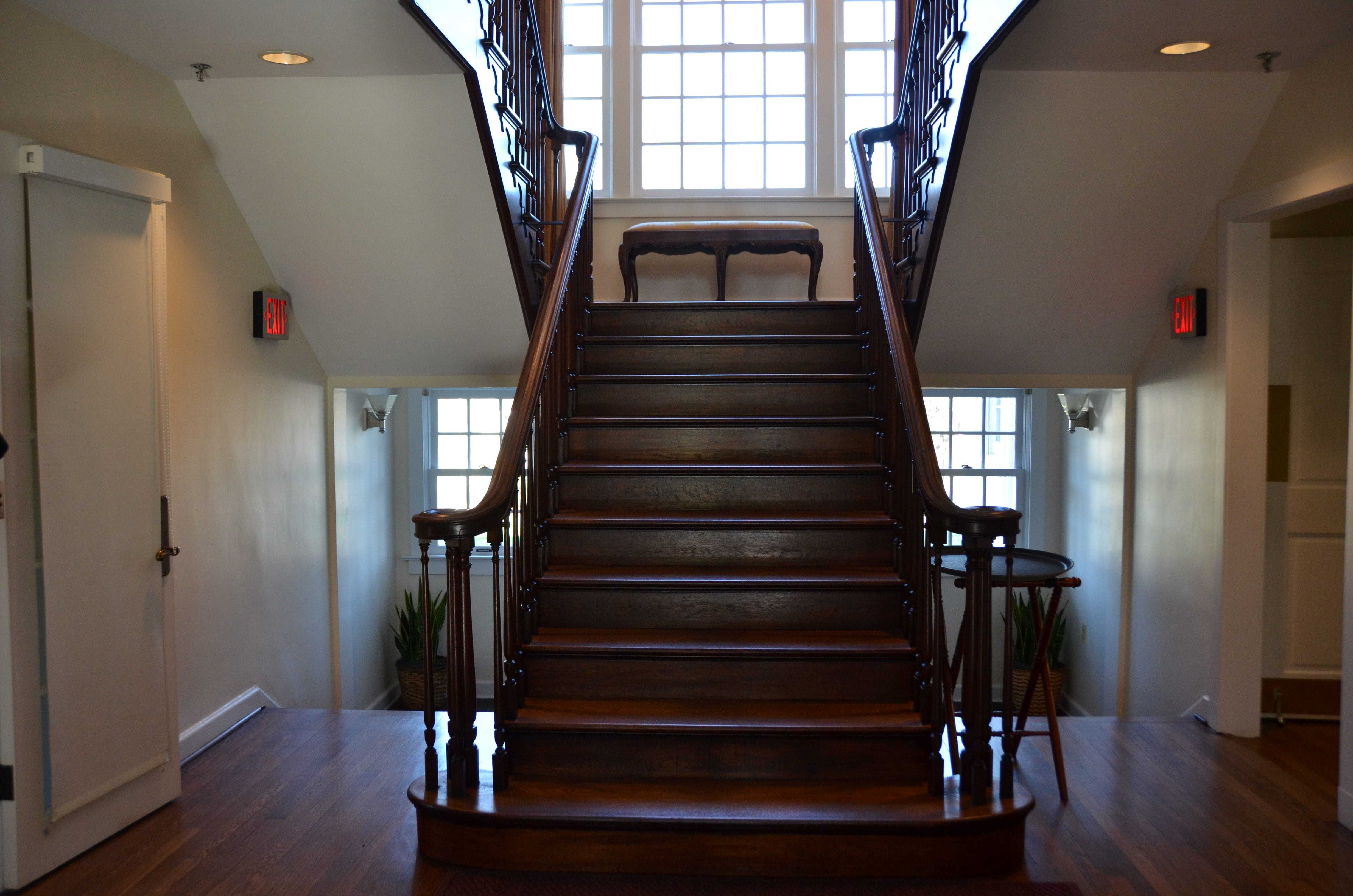 A dark wooden staircase at the entrance of the manor house leading to another set of stairs.